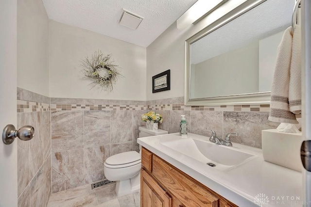 bathroom featuring a wainscoted wall, visible vents, toilet, vanity, and tile walls