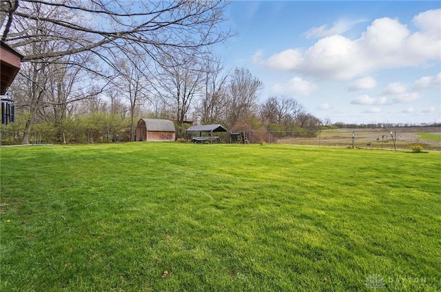 view of yard with fence, a shed, a rural view, an outdoor structure, and a detached carport