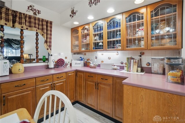 kitchen with light countertops, white microwave, brown cabinets, and tasteful backsplash