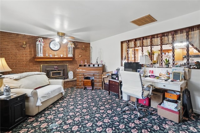 carpeted office space featuring brick wall, a ceiling fan, visible vents, and a fireplace