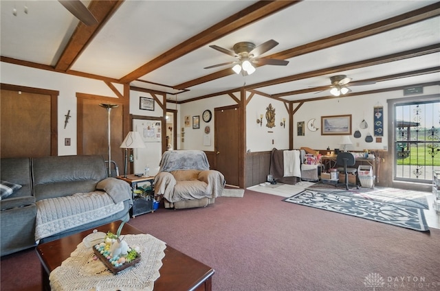 living room with carpet flooring, a ceiling fan, a wainscoted wall, and beam ceiling