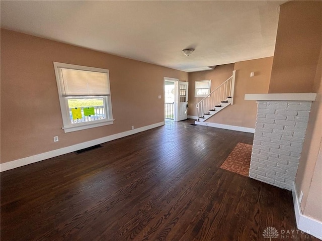 unfurnished living room with dark wood-style floors, baseboards, stairs, and visible vents