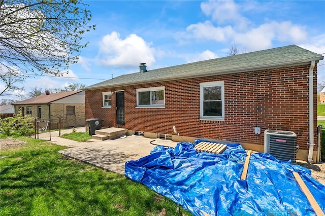 back of property with central AC unit, a shingled roof, fence, a patio, and brick siding