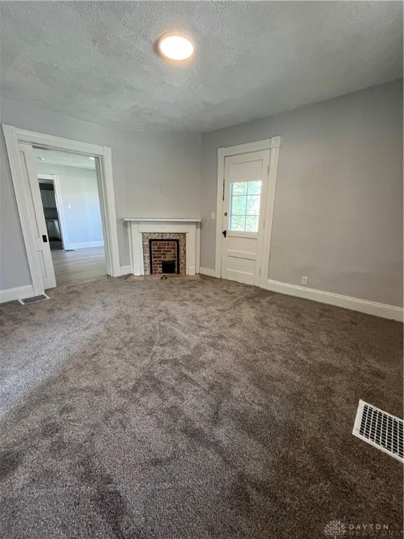 400 S Detroit St, Xenia, OH 45385 - unfurnished living room with a textured ceiling, baseboards, carpet floors, and a fireplace with flush hearth