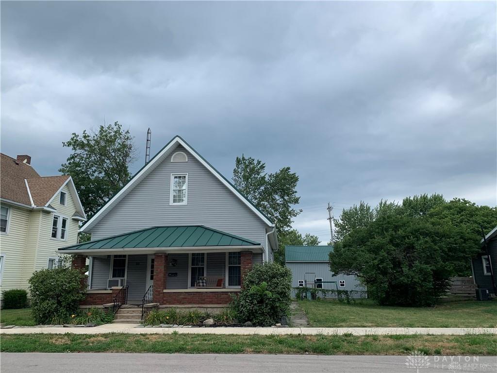 bungalow-style house featuring a standing seam roof, covered porch, brick siding, a front yard, and metal roof