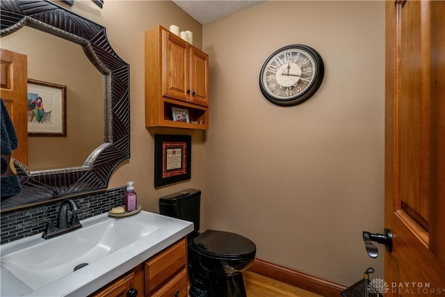 half bathroom featuring wood finished floors, decorative backsplash, vanity, baseboards, and toilet