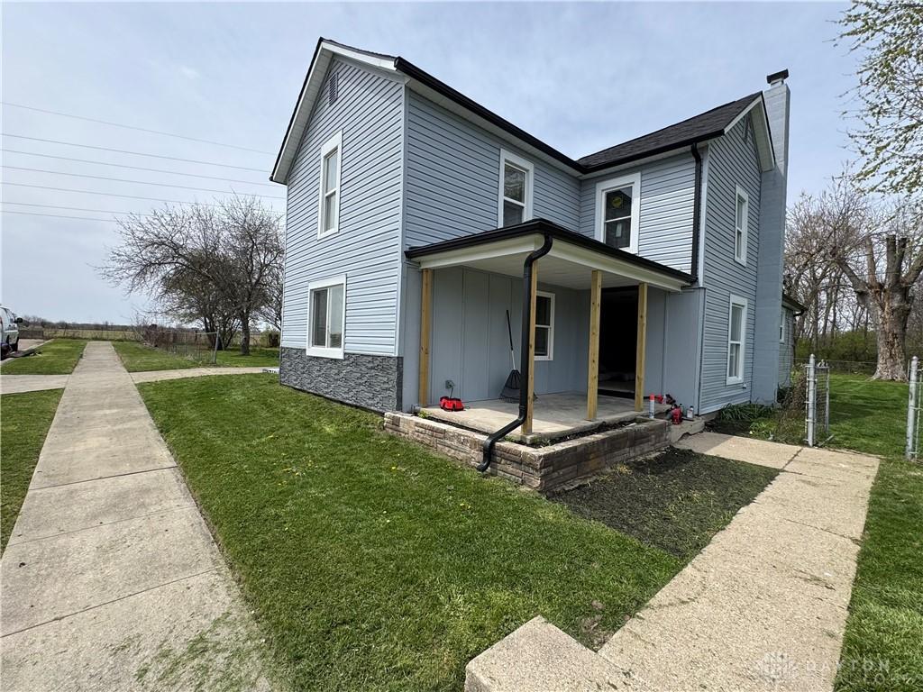 view of front facade with board and batten siding, a front lawn, a chimney, and covered porch