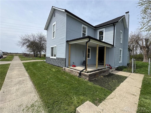 view of front facade with board and batten siding, a front lawn, a chimney, and covered porch