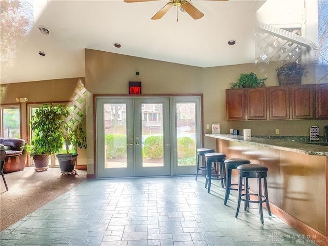 kitchen with a breakfast bar, french doors, stone tile flooring, brown cabinetry, and ceiling fan