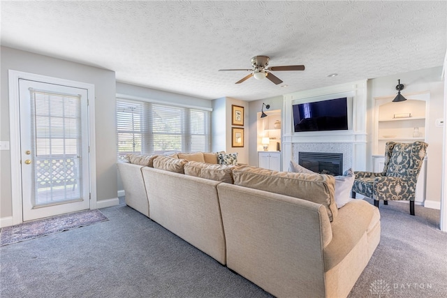 carpeted living area with baseboards, a glass covered fireplace, a textured ceiling, and ceiling fan