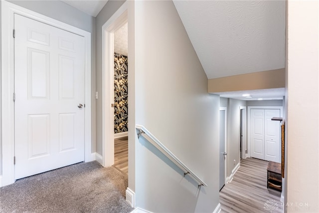 corridor with a textured ceiling, an upstairs landing, carpet floors, baseboards, and lofted ceiling