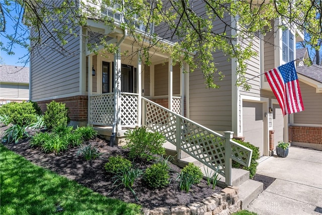 property entrance with brick siding, a porch, concrete driveway, and a garage