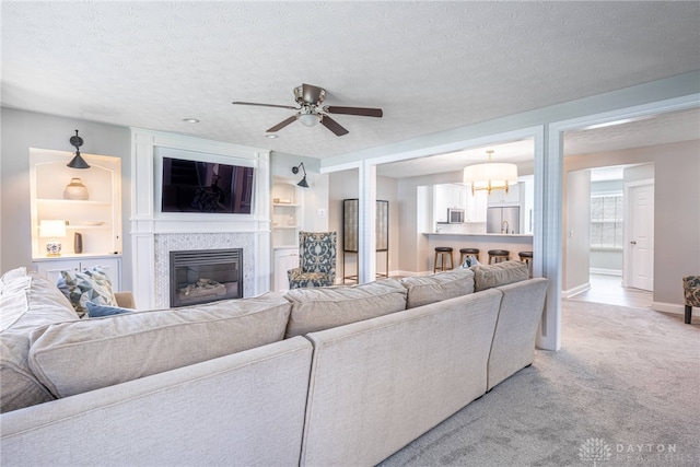 living area featuring a textured ceiling, ceiling fan, a fireplace, light colored carpet, and baseboards