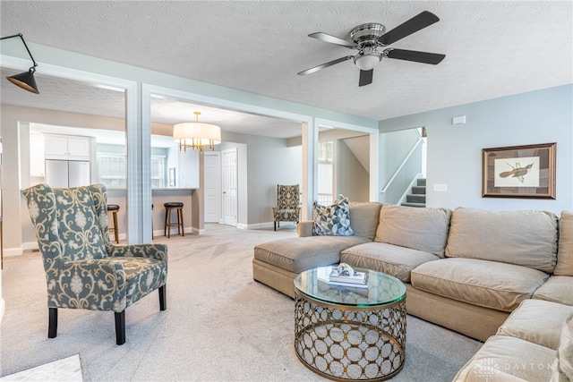 living room featuring light colored carpet, baseboards, a textured ceiling, stairs, and ceiling fan with notable chandelier