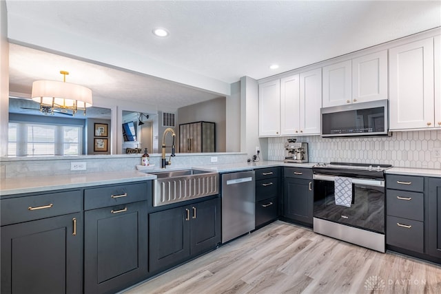 kitchen featuring stainless steel appliances, light countertops, a sink, light wood-style flooring, and white cabinetry