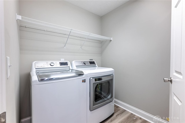 clothes washing area featuring washing machine and clothes dryer, light wood-style floors, laundry area, and baseboards