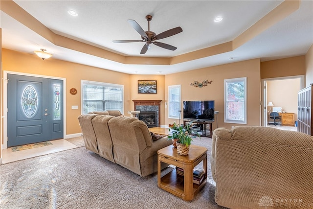 living room with carpet flooring, ceiling fan, a raised ceiling, a glass covered fireplace, and recessed lighting