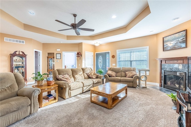living area with a raised ceiling, a ceiling fan, carpet flooring, and visible vents