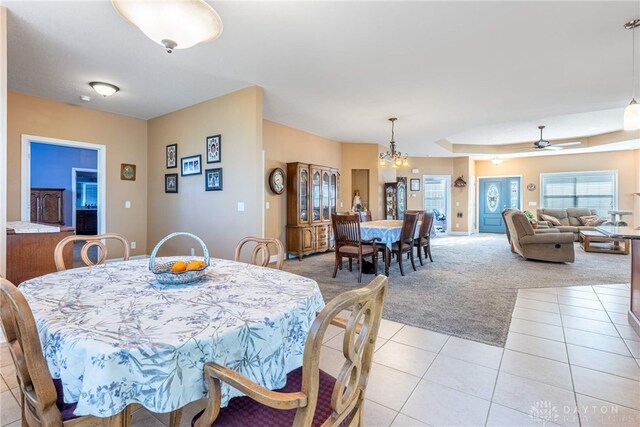 dining area featuring light colored carpet, a raised ceiling, ceiling fan with notable chandelier, and light tile patterned floors
