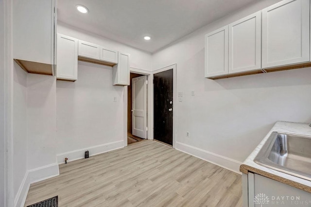 kitchen with white cabinets, light wood-style flooring, baseboards, and a sink