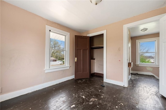 unfurnished bedroom with wood-type flooring, baseboards, multiple windows, and a closet