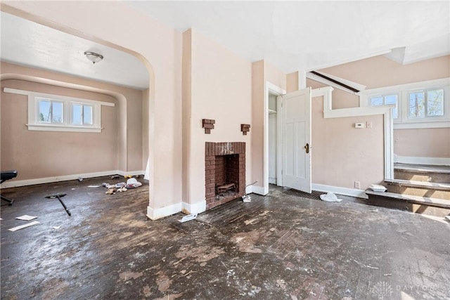 unfurnished living room with a fireplace, arched walkways, and baseboards