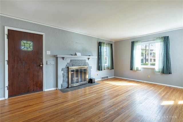 unfurnished living room featuring hardwood / wood-style floors, a textured wall, visible vents, crown molding, and a fireplace