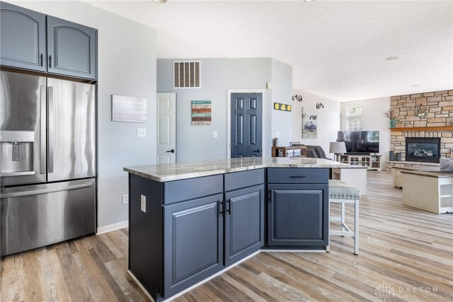 3513 Black Squirrel Way, Springboro, OH 45005 - kitchen featuring stainless steel refrigerator with ice dispenser, light wood-style floors, a center island, light stone countertops, and a fireplace