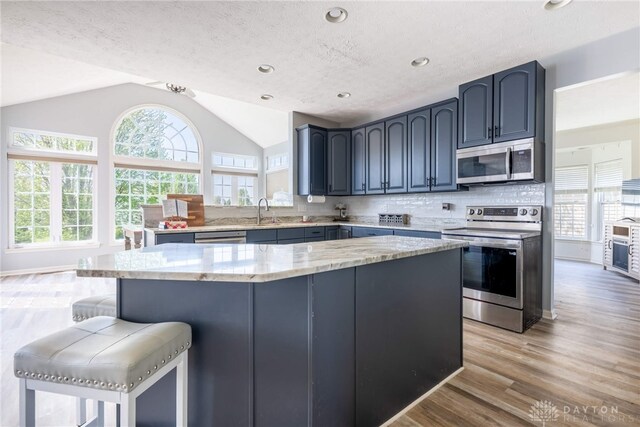 3513 Black Squirrel Way, Springboro, OH 45005 - kitchen featuring appliances with stainless steel finishes, vaulted ceiling, light stone countertops, light wood-style floors, and a kitchen breakfast bar