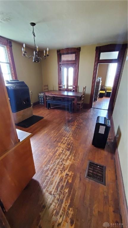 interior space featuring baseboards, visible vents, an inviting chandelier, wood finished floors, and a wood stove