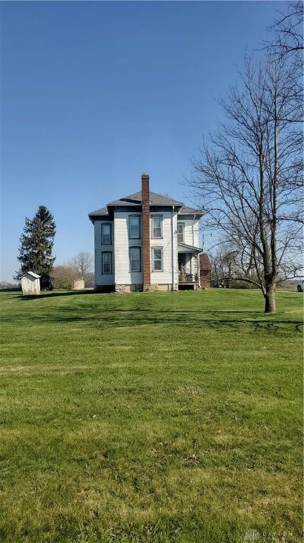back of property featuring a chimney, an outdoor structure, a yard, and a storage unit