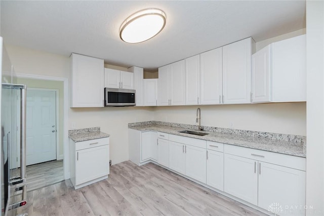 kitchen featuring light stone counters, a sink, stainless steel microwave, light wood-type flooring, and white cabinetry