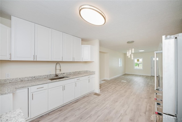 kitchen featuring light wood-style flooring, a sink, baseboards, a chandelier, and white cabinetry