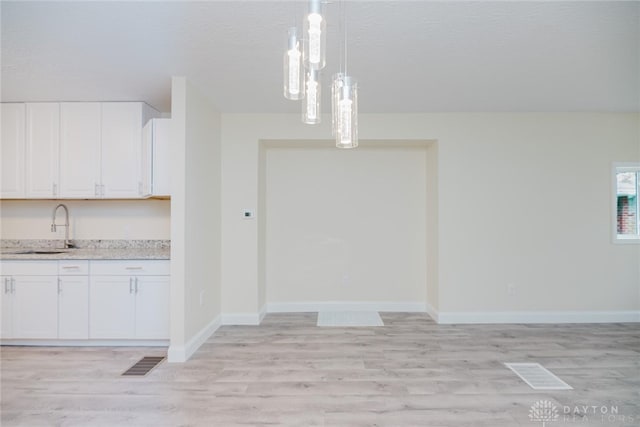 unfurnished dining area featuring baseboards, light wood finished floors, a sink, and visible vents