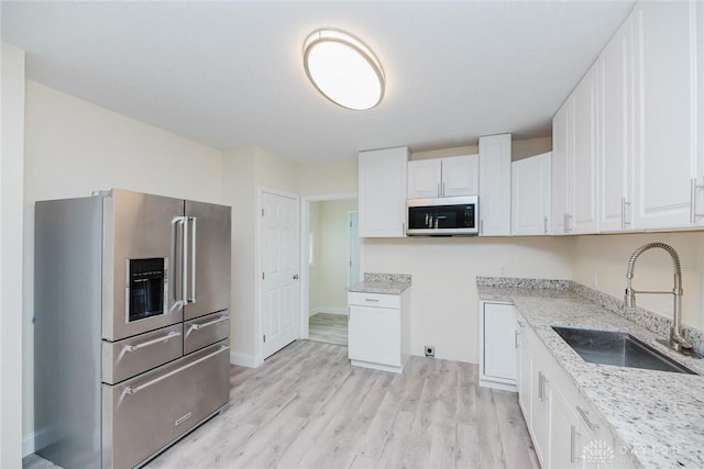 kitchen with white cabinets, a sink, light wood-style floors, light stone countertops, and appliances with stainless steel finishes