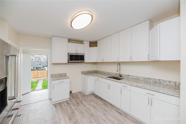 kitchen with light wood-style flooring, a sink, white cabinetry, and appliances with stainless steel finishes