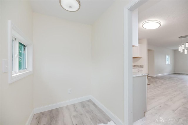 corridor with baseboards, a chandelier, and light wood-style flooring
