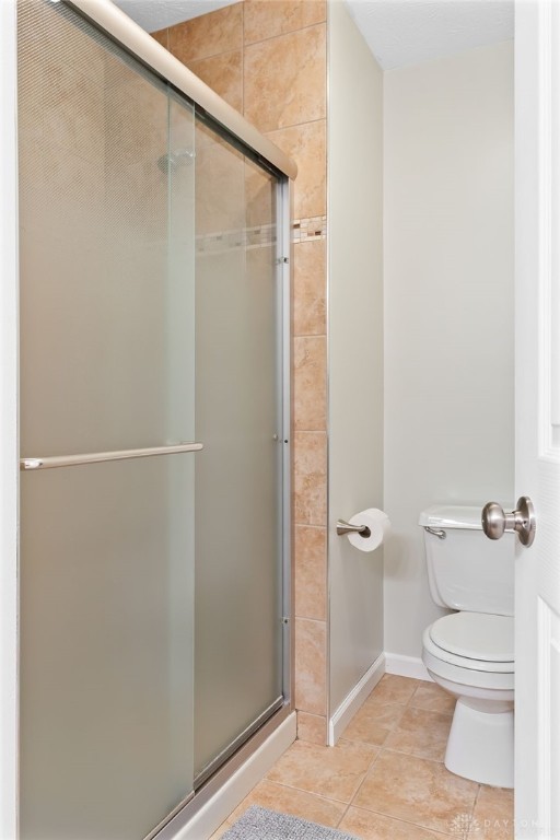 bathroom with tile patterned flooring, a shower stall, toilet, and baseboards