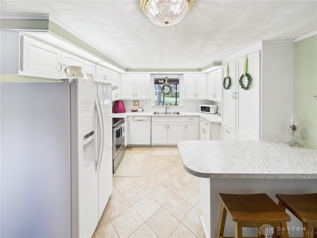 kitchen featuring a breakfast bar, backsplash, a sink, white appliances, and a peninsula