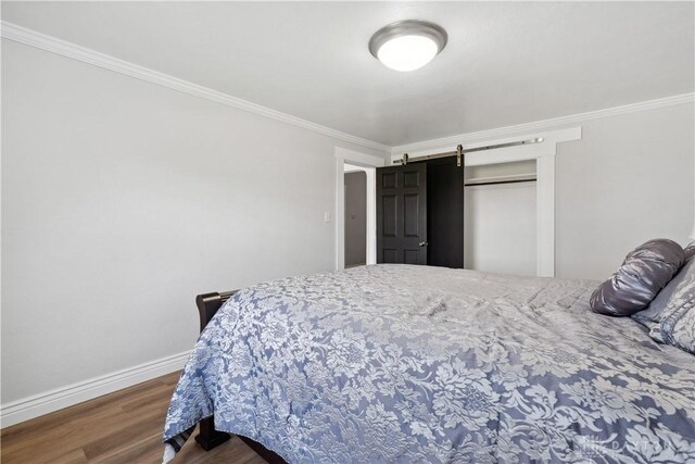 bedroom featuring a barn door, baseboards, crown molding, and wood finished floors
