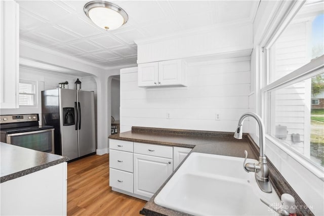kitchen with stainless steel appliances, dark countertops, a sink, arched walkways, and white cabinetry