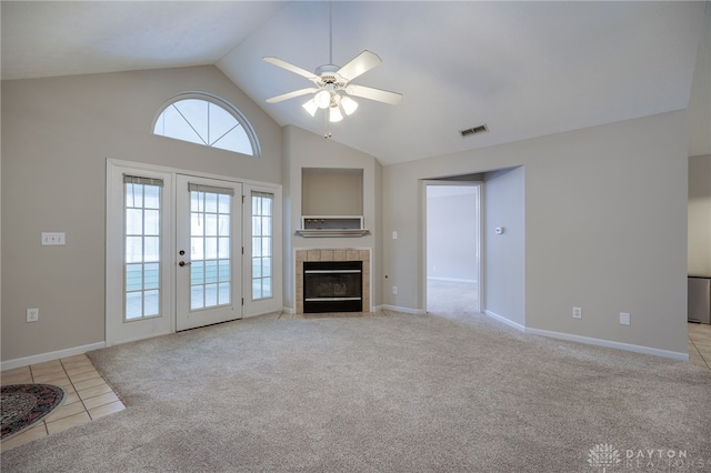 unfurnished living room with a tile fireplace, visible vents, light colored carpet, high vaulted ceiling, and ceiling fan