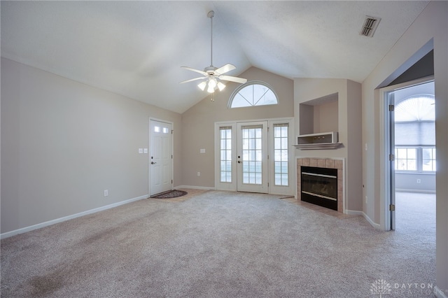 unfurnished living room with vaulted ceiling, ceiling fan, a tile fireplace, carpet, and visible vents
