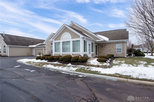 view of snowy exterior featuring a garage, stone siding, and aphalt driveway