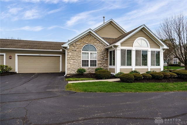 ranch-style house featuring an attached garage, driveway, stone siding, and roof with shingles