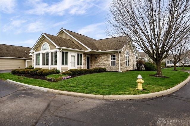 view of side of property with stone siding, a lawn, and a shingled roof