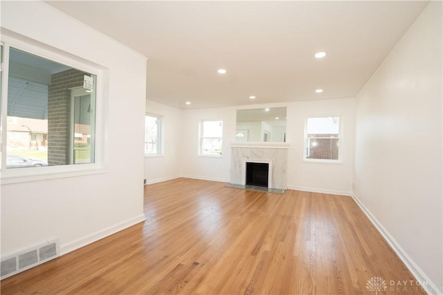 unfurnished living room with baseboards, light wood-style floors, visible vents, and a premium fireplace