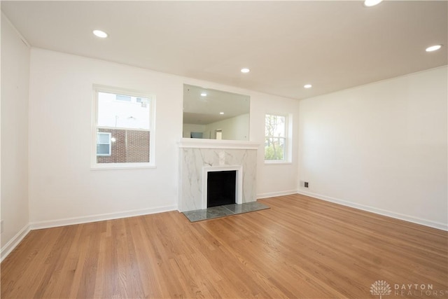 unfurnished living room with recessed lighting, a premium fireplace, wood finished floors, and baseboards
