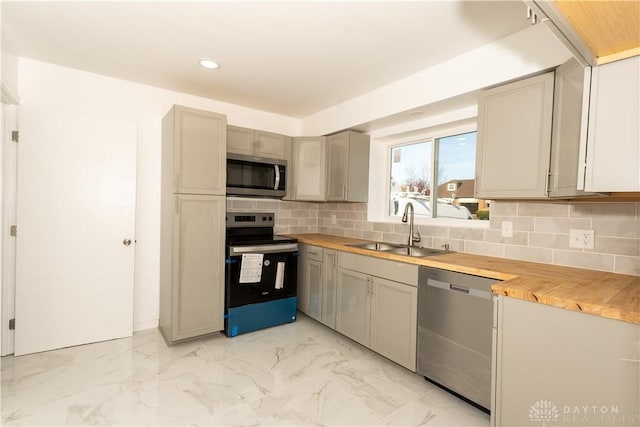 kitchen featuring backsplash, appliances with stainless steel finishes, a sink, and butcher block countertops