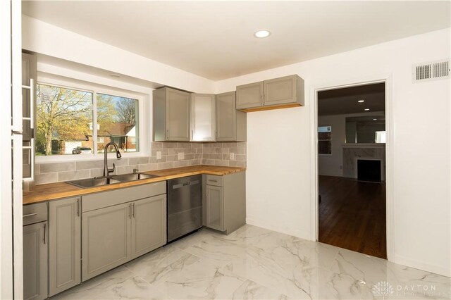 kitchen featuring stainless steel dishwasher, gray cabinetry, a sink, and visible vents